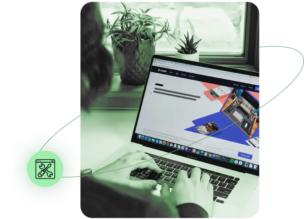 Person arbeitet an einem Laptop, auf dessen Bildschirm die Shopify-Website geöffnet ist. Im Hintergrund stehen Pflanzen auf der Fensterbank. Links unten befindet sich ein grünes Symbol mit einem Browserfenster und Werkzeugen, das umfangreiche Anpassungsmöglichkeiten und Designfreiheit symbolisiert.